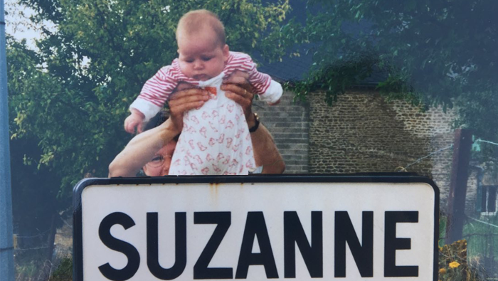 Suzanne as a baby, being held over a sign sayng Suzanne